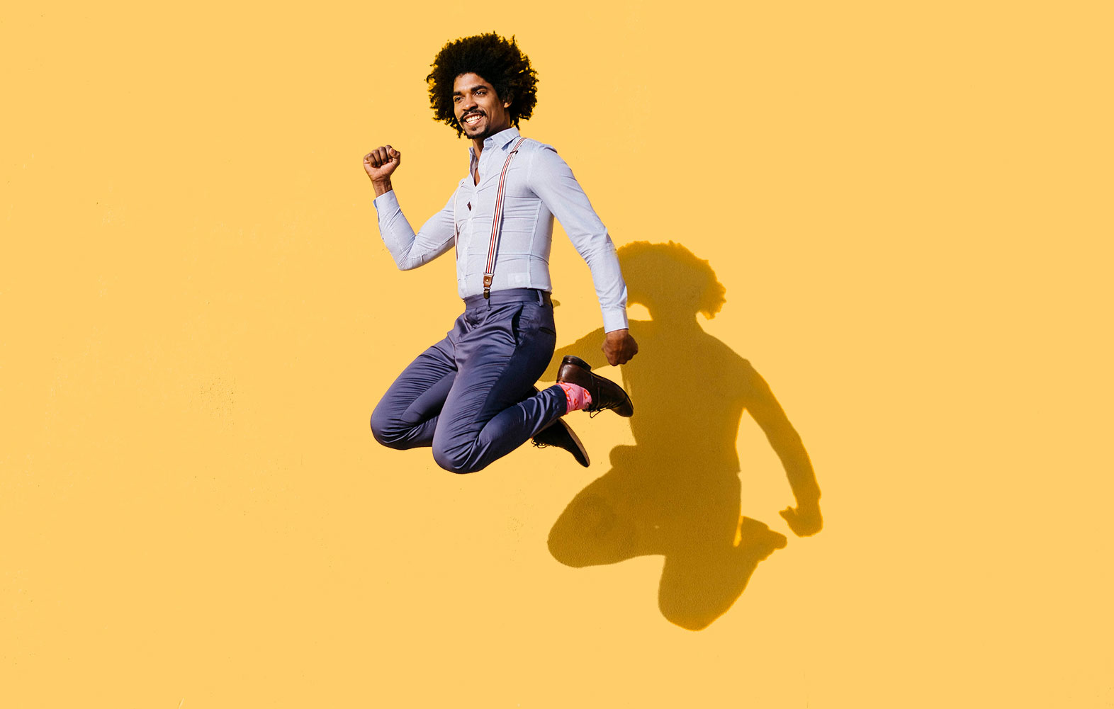 A man in suspenders jumping in the air behind a yellow background